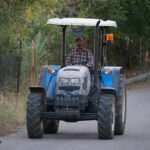 farmer driving blue tractor on rural road